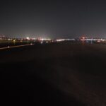 Night view of an airport runway with distant city lights and runway lights visible in the background.